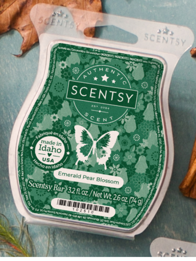 A green labeled Scentsy Wax Melt in the Emerald Pear Blossom fragrance sits on a blue tablecloth.