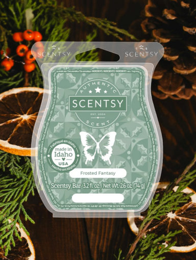 Scentsy's Frosted Fantasy Wax Bar clam shell with green label sits on top of pine branches and slices of dried bergamot.