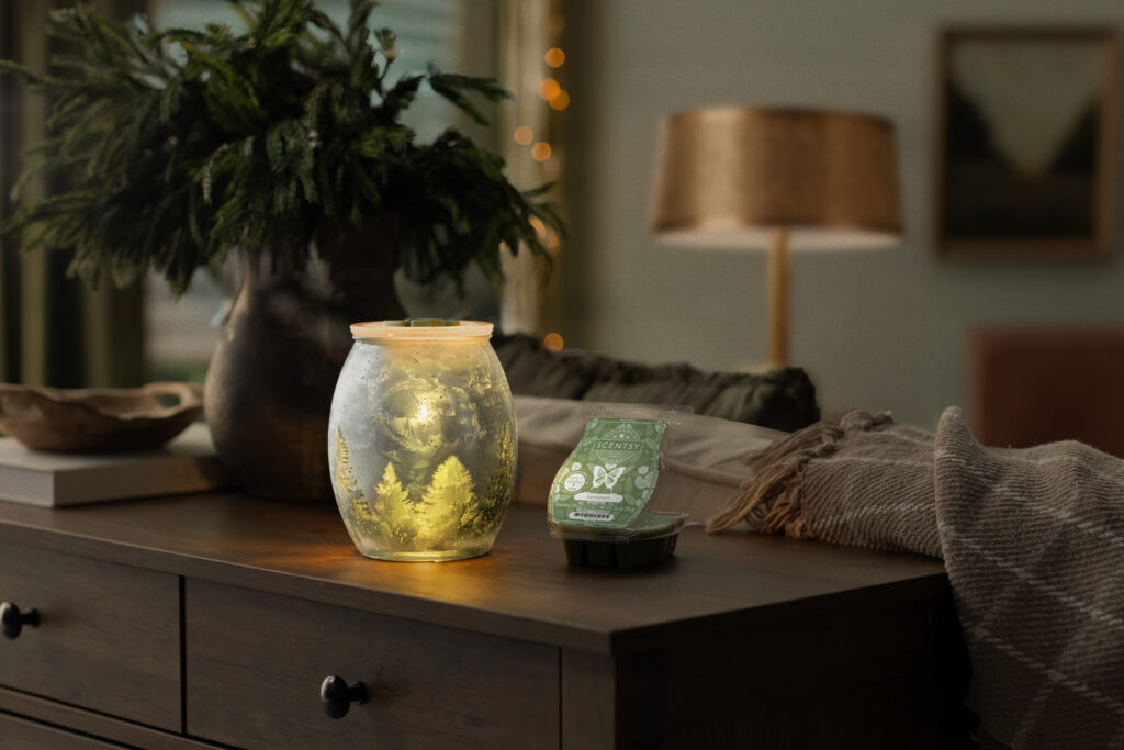 Scentsy's Scent and Warmer of the Month, Wintercrest Wax Warmer and Iced Balsam Scented Wax Melt, sit beside a houseplant on dark brown living room sofa table.