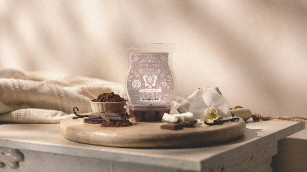 Scentsy's Scent of the Month, Cocoa Cashmere, sits on a marble mantle surrounded by vanilla blossoms, chocolate, and a wool blanket in the background.