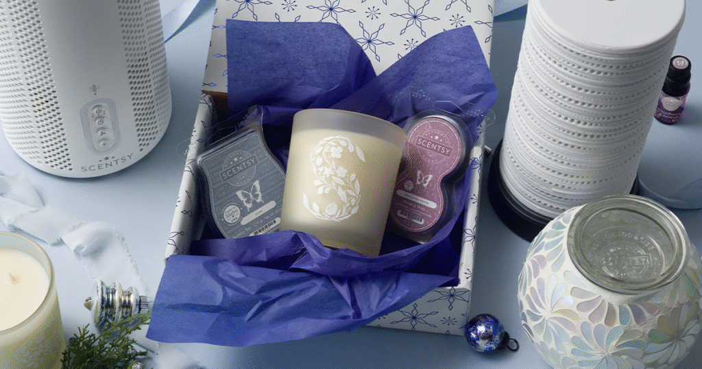 A Scentsy Gift Set Christmas gift box containing a Scentsy Wax Bar, Scented Candle, and Scentsy Pod, wrapped in blue tissue paper and snowflake-patterned Christmas wrapping paper. The Christmas gift is surrounded by a Scentsy Air Purifier, Wax Warmer, and Cartridge Oil Diffuser. 