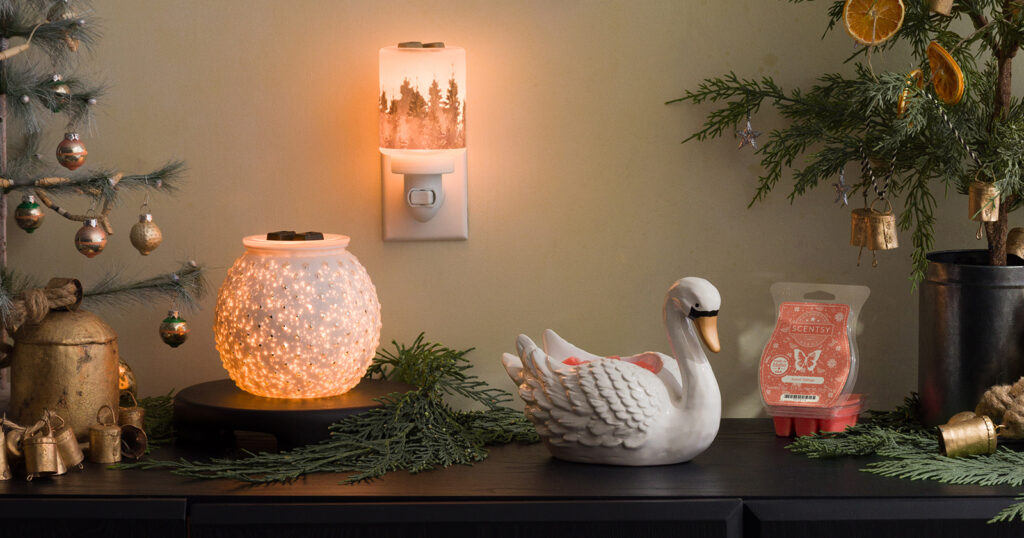 The Scentsy Winter Swan and Snow Drop Warmers, Evergreen Pine Mini Warmer, and Sweet Tidings Wax Bar from the All is Calm Holiday Collection sit on a warmly lit hallway table surrounded by small, decorated Christmas trees with vintage gold ornaments. 