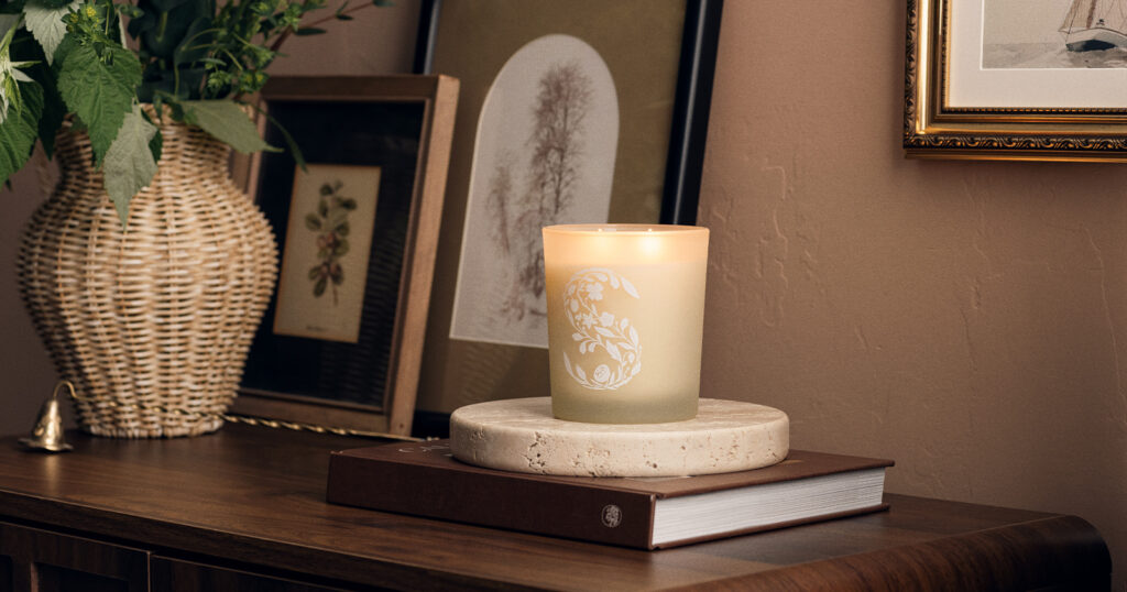 A Scentsy Candle sits on a table beside photographs, house plants, and books. 