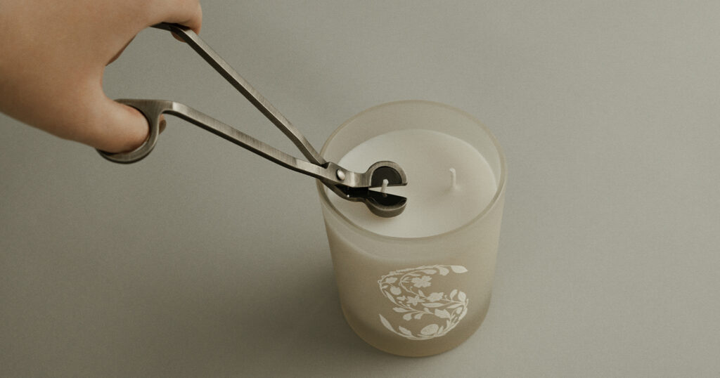 Depicts a hand holding candle wick trimmers preparing to trim the wick on an unlit Scentsy candle. 