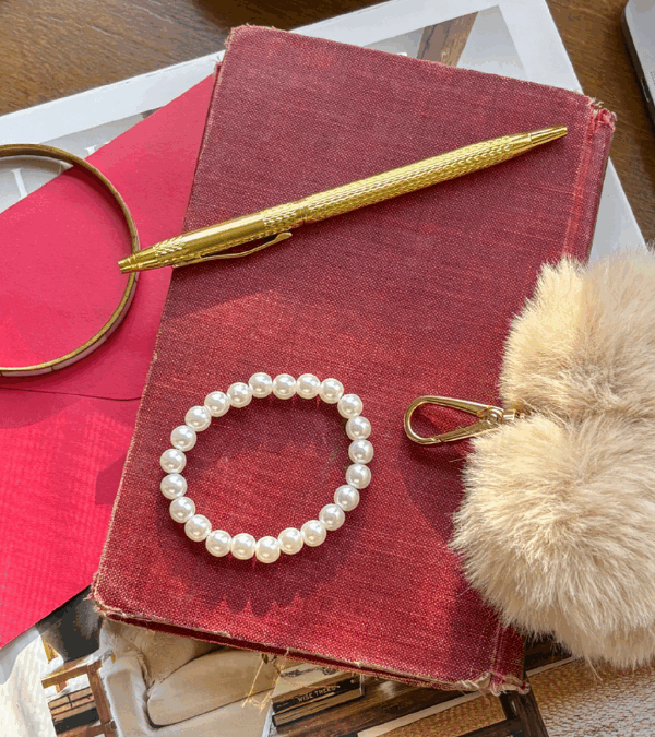 A heart Scentsy Charm Clip sits atop a red journal and red stationary scattered about a desk.