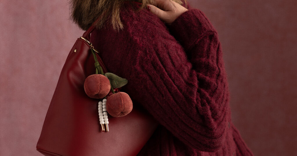A woman wears the Scentsy Santina Cherry Charm Clip attached to her purse. 