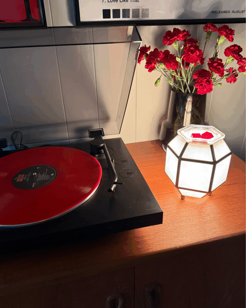 A red record sits on a record player beside a vase of valentines day roses and the Clara Scentsy Wax Warmer with red wax melts in the dish.