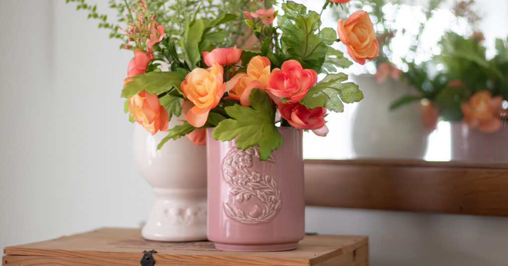 A pink ceramic Scentsy Candle, upcycled as a DIY vase, holds a bouquet of orange flowers. 