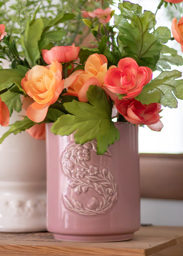 A pink ceramic Scentsy Candle, upcycled as a DIY vase, holds a bouquet of orange flowers.