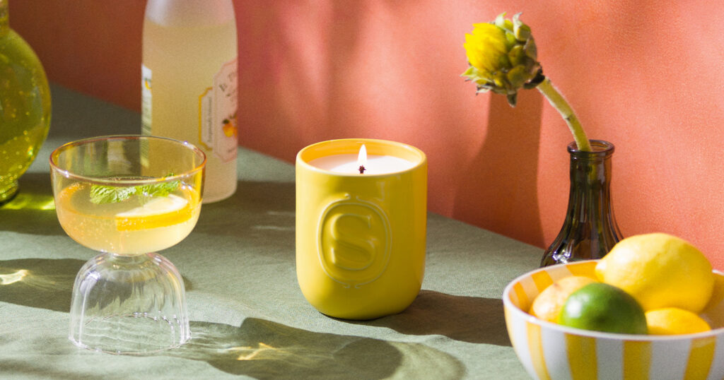 A Limone Fresco Scentsy Candle is lit in a mediterranean kitchen setting with citrus fruits and a fresh beverage.