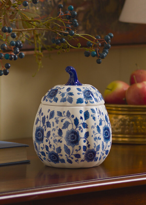 A Scentsy Indigo Vine Pumpkin Warmer is displayed on an entry table next to a lamp, bowl of apples and fall decor. Wax melts in this warmer create cozy fall scents.