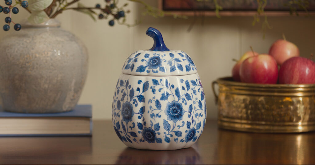 An Indigo Vines Pumpkin Warmer on a hall table near apples, ideal for warming wax melts in cozy fall fragrances.